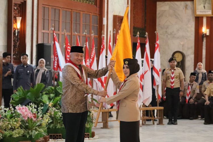 Gubernur H. Muhidin menyerahkan bendera kontingen kepada Ketua Kwartir Daerah Gerakan Pramuka Kalsel, Hj. Fathul Jannah Muhidin saat melepas peserta Jambore Nasional XII Tahun 2026.